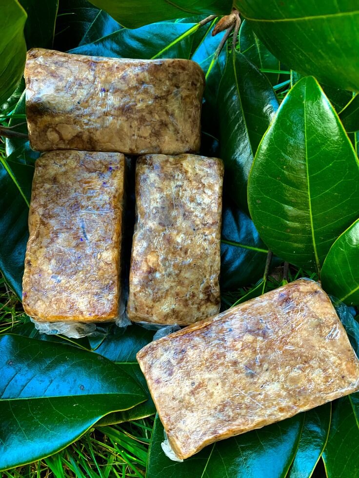 Four wrapped bars of Nia Glow African Black Soap on green leaves